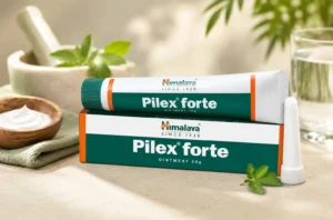 Himalaya Pilex Forte Ointment 30g tube and box displayed on a table with an applicator nozzle, fresh herbs, a mortar and pestle, and a glass of water.